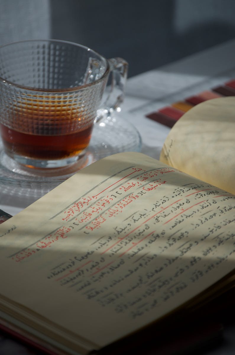 Artistic still life featuring an open book with Arabic script beside a clear glass of tea.